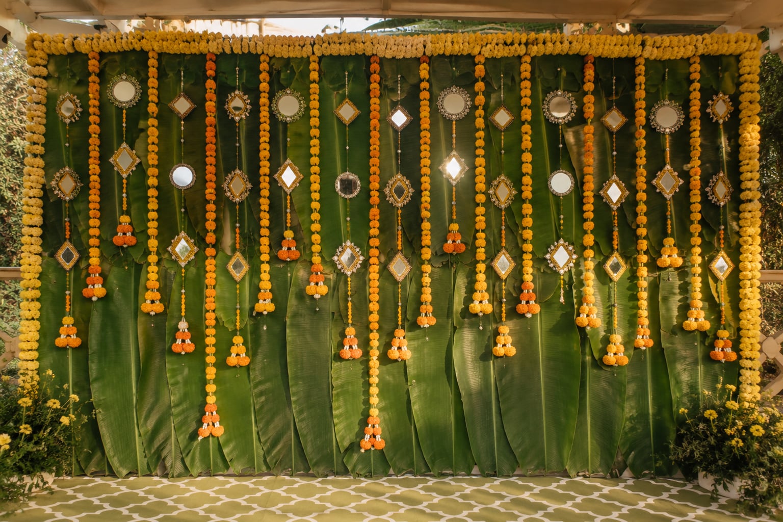 Banana-leaf and marigold backdrop with hanging mirror-work