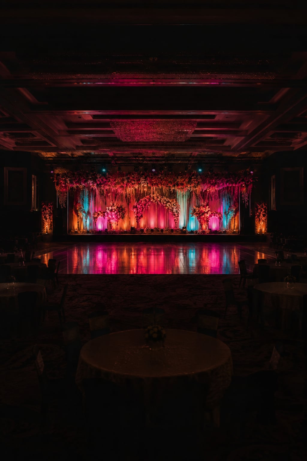 The lit stage seen small within the dark hall, tables in silhouette